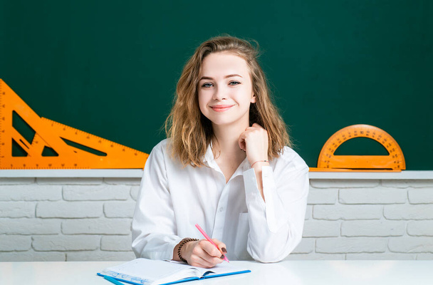 Happy teenager studying in classroom. Young attractive student with books in white uniform school shirt. School girl ready to homework. - Foto, Bild
