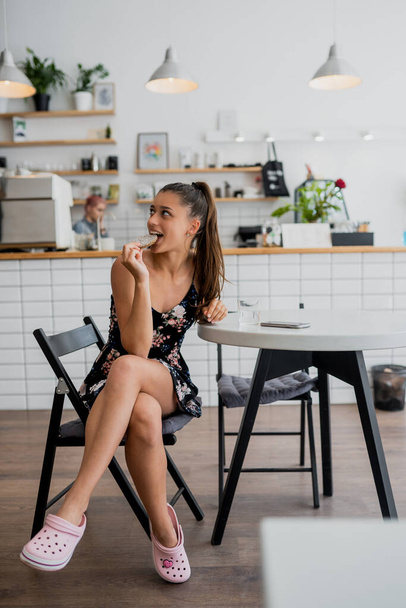 Счастливая улыбающаяся девушка держит печенье в уютном кафе. - Фото, изображение