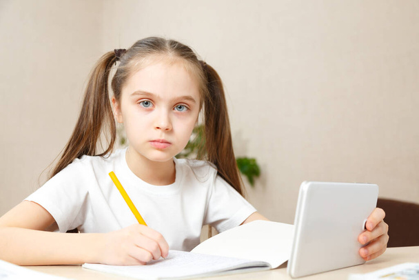 Kształcenie online na odległość. Uczennica studiuje w domu z notebookiem i robi pracę domową.Dziewczyna robi pracę domową z radością i zainteresowaniem. Odległość społeczna podczas kwarantanny - Zdjęcie, obraz