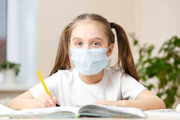 The school girl is studying at home, studying at home during quarantine, masked child studying at home - Foto, Bild