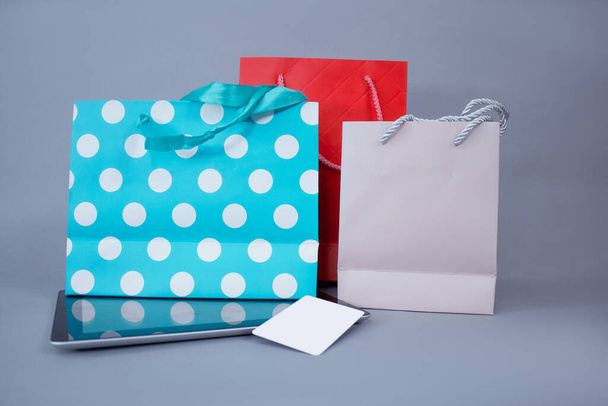 Online shopping concept. Close-up tablet mockup with white screen and credit card against the background of bright gift bags - Foto, imagen
