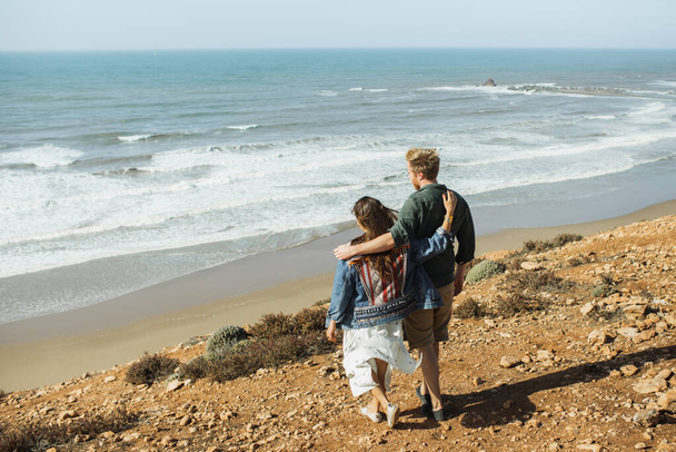 Νεαρό κομψό αγνώριστο ζευγάρι περπάτημα με καταπληκτική θέα στον ωκεανό. Πίσω όψη από πίσω. Ταξιδιωτική ιδέα, μέρος για κείμενο. Μήνας του μέλιτος στις τροπικές περιοχές. - Φωτογραφία, εικόνα