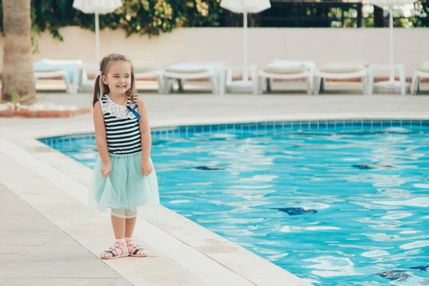 A little girl walks by the pool. Holidays in hot countries. the territory of the hotel - Фото, изображение