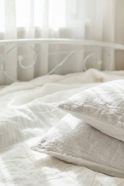 Beyaz keten çarşaflar. Yastık yığını. Konforlu yatak odası içi ve güzel sabah ışığı. Pastel renk. Moda organik doğal keten. - Fotoğraf, Görsel
