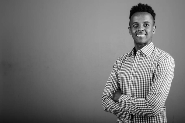 Studio shot of young handsome African businessman wearing checkered shirt against gray background in black and white - Foto, immagini
