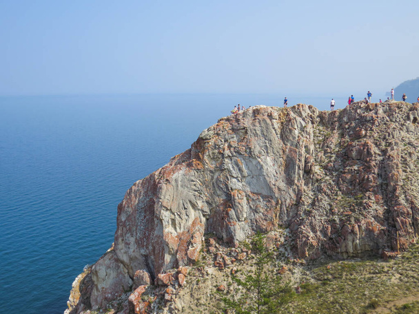 Tourists on the top of the cliff of Olkhon Island. View of Lake Baikal in summer. - Photo, Image