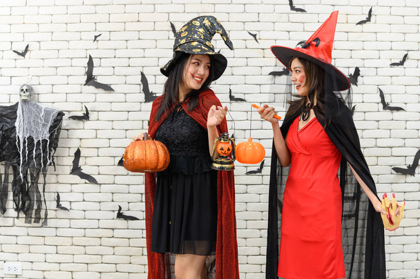 ハロウィンのために装飾された背景にカボチャジャックOランタンを保持魔女の衣装を身に着けている2人の美しい若いアジアの女性の肖像 - 写真・画像