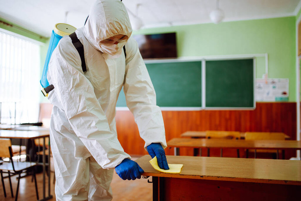 消毒グループの男が黄色の布で学校の机を掃除します。プロの作業員が教室を滅菌し、コヴィト-19の拡散を防ぎます。学生・学生の健康管理の考え方 - 写真・画像