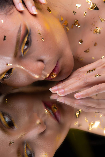 Πορτρέτο της μόδας 20s Ασιατική γυναίκα έχει όμορφη ενημέρωση συνθέτουν καλλιτέχνη στο πινέλο, αυτή διακοσμούν με μοντέρνα φύλλα χρυσού στο κεφάλι πρόσωπο και αντανακλούν καθρέφτη, αντίγραφο χώρο - Φωτογραφία, εικόνα