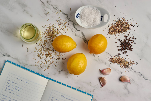 A top view of a marble table with a notebook with a recipe, lemon, garlic, and spices - Фото, зображення