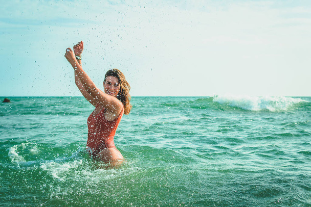 A beautiful European female with an orange swimsuit having fun at sea - Photo, image