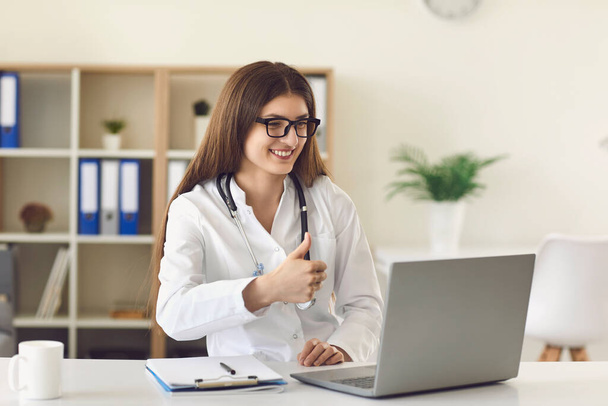 Online medical service. Female doctor showing thumb up gesture to patient on web. GP talking to client on laptop - Foto, Bild