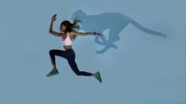 Wild. Full length shot of young sportive mixed race woman looking focused while jumping, running isolated over pale blue creative art background with cheetah shadow. Sports and workout concept - Фото, зображення