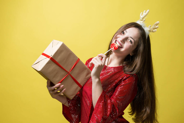 Une fille dans une robe rouge avec des cadeaux sur un fond jaune. - Photo, image