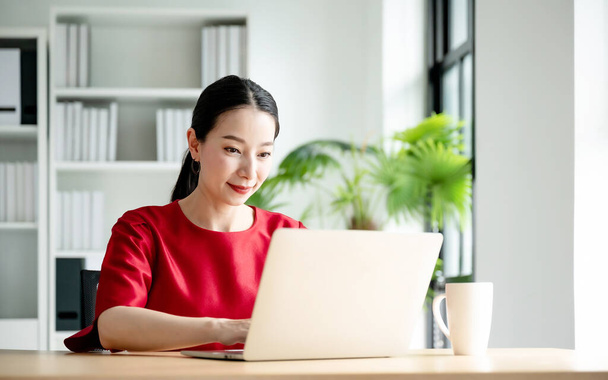 Arbeit zu Hause, Videokonferenz, Online-Videotelefonie, Porträt einer schönen jungen asiatischen Frau, die auf dem Computerbildschirm Webinar anschaut und am Laptop am Arbeitsplatz arbeitet - Foto, Bild