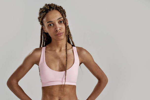 Portrait of young sportive mixed race woman in sportswear looking at camera while posing isolated over grey background. Healthy lifestyle and sports concept - Photo, image