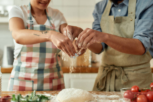 Felvágott kép a párokról, ahogy együtt készítik a tésztát. Fiatal férfi és nő kötényben főz, otthon pizzát készít. Hobbi, életmód - Fotó, kép