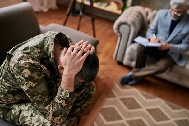 Remove your memories. Middle aged military man holding his head in pain and depression during therapy session with psychologist. Soldier suffering from psychological trauma. PTSD concept - Foto, Imagem