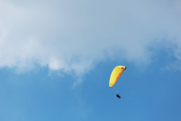 Sarı paraglider, güneşli bir günde bulutlarla mavi gökyüzüne doğru uçuyor.. - Fotoğraf, Görsel