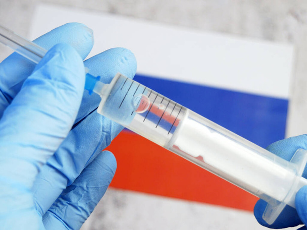 ruiskua rokotteella pidetään käsin käsineessä Venäjän federaation lipun taustalla, rokote koronavirusta vastaan, operaatio Poimunopeus - Valokuva, kuva