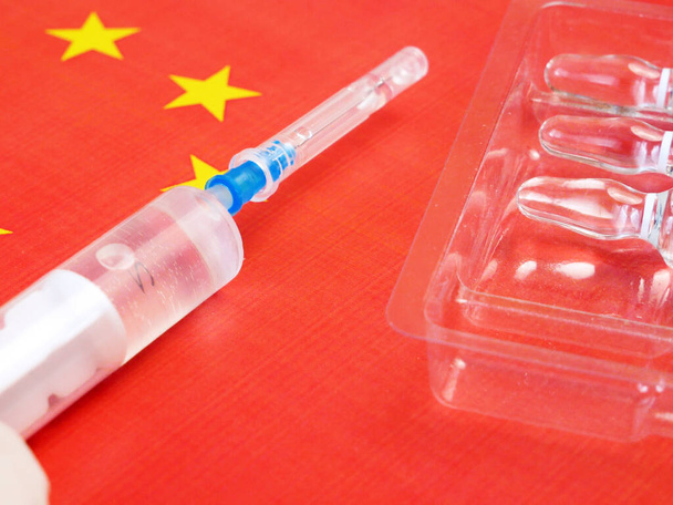 jeringa con una vacuna se sostiene a mano en un guante en el fondo de la bandera china, vacuna contra el coronavirus, Operación Velocidad Warp - Foto, imagen