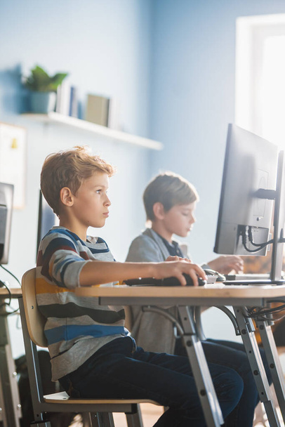 Elementary School Computer Science Classroom: Smart Little Schoolboy Works on Personal Computers, Learning Programming Language for Software Coding. Schoolchildren Getting Modern Education. - 写真・画像