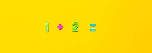 Wiskundig voorbeeld één plus twee is gelijk aan een gele achtergrond gemaakt van plastic kindernummers. De eerste stappen in het beheersen van wiskunde op de basisschool. Eenvoudige actie en oplossing. Helder spandoek - Foto, afbeelding