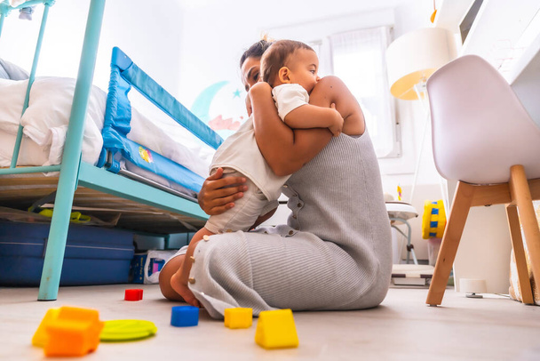 Young Caucasian mother playing with her in the room with toys. Baby less than a year learning the first lessons of her mother. Mother playing with her son and hugging him lovingly - Foto, Bild
