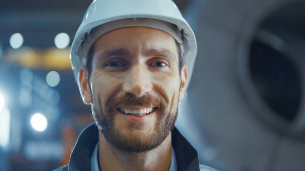 Portrait of Smiling Professional Heavy Industry Engineer Worker Wearing Safety Uniform and Hard Hat. In the Background Unfocused Large Industrial Factory - Fotoğraf, Görsel
