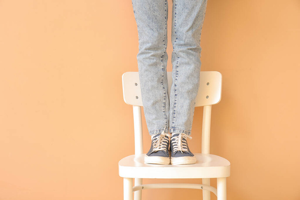 Schöne junge Frau in Jeans-Kleidung auf Stuhl vor farbigem Hintergrund - Foto, Bild