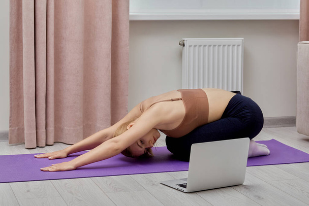 Young woman is engaged in yoga and sports near the laptop. - Valokuva, kuva