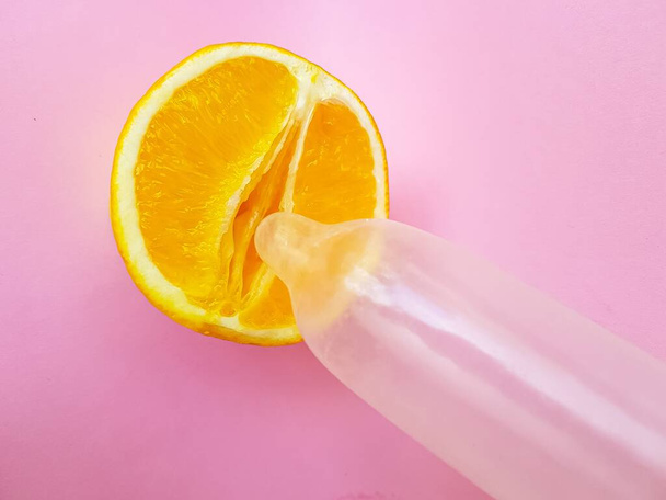 The concept of safe sex and protection. A vagina symbol. A juicy orange and a condom on a bright pink background. - Fotó, kép