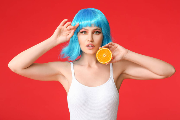 Mulher bonita em peruca e com laranja sobre fundo de cor - Foto, Imagem