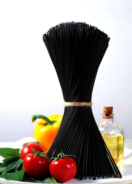 un bouquet de spaghettis noirs, une composition des ingrédients de la cuisine italienne, verticale, fond blanc  - Photo, image