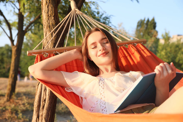 Jeune femme lisant le livre tout en se relaxant dans l'hamac dehors - Photo, image