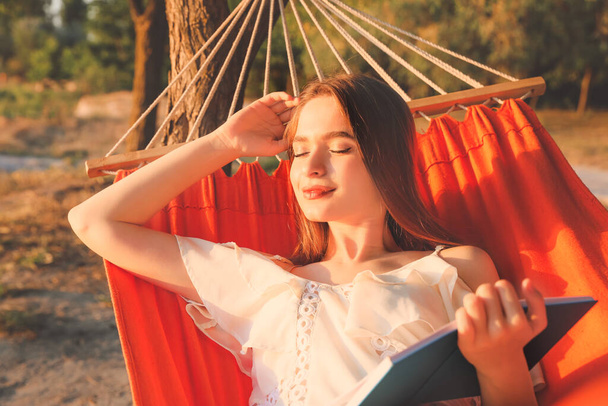 Joven mujer leyendo libro mientras se relaja en hamaca al aire libre - Foto, imagen