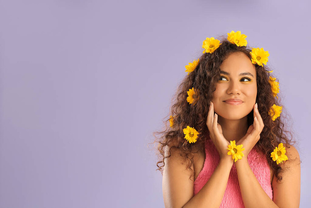 Giovane donna afro-americana con bellissimi ombretti e fiori nei capelli sullo sfondo di colore - Foto, immagini