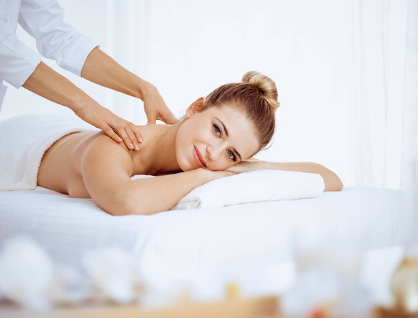 Young and blonde woman enjoying massage of back in spa salon. Beauty concept - Foto, immagini