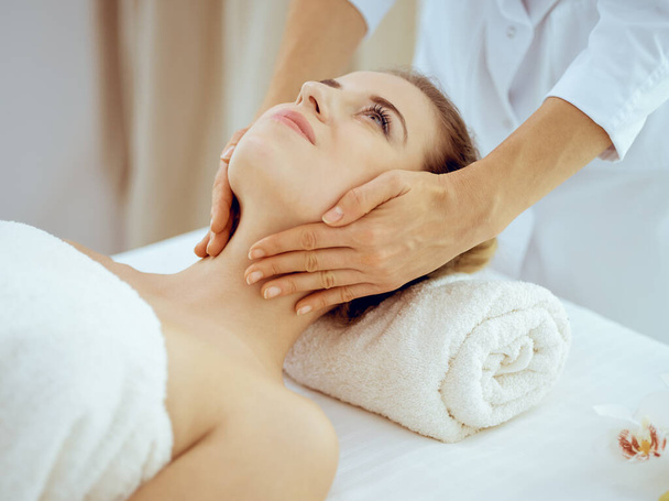 Young and blonde woman enjoying facial massage in spa salon. Beauty concept - Valokuva, kuva