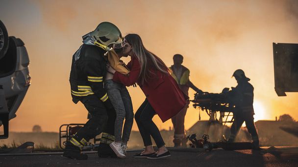 Brave Firefighter Carries Injured Young Girl to Safety where She Reunited with Her Loving Mother. In the Background Car Crash Traffic Accident Courageous Paramedics and Firemen Save Lives - Foto, Bild