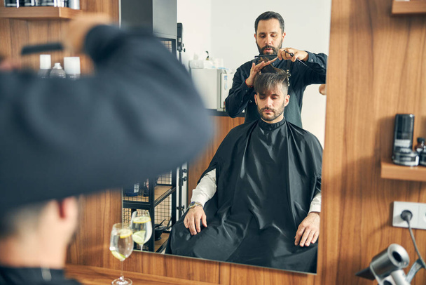 Concentrated barber doing stylish haircutting for his client - Fotó, kép