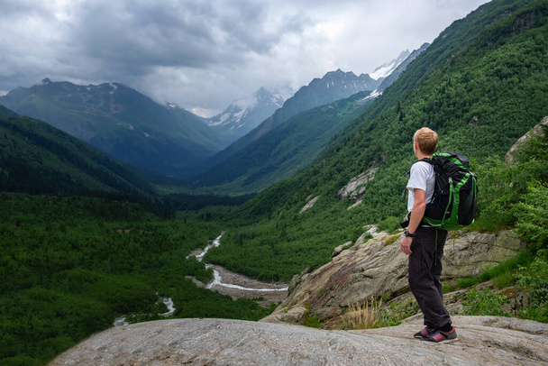 Ağır sırt çantasıyla dağlarda yürüyüş yapan bir adam. Seyahat tarzı seyahat macera macerası konsepti, yaz tatili vahşi doğada tek başına. Kuzey Kafkasya, Dombai, Rusya. - Fotoğraf, Görsel
