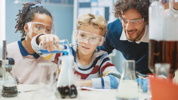 Elementary School Science Classroom: Little Boy Mixes Chemicals in Beakers. Enthusiastic Teacher Explains Chemistry to Diverse Group of Children. Children Learn with Interest - Zdjęcie, obraz