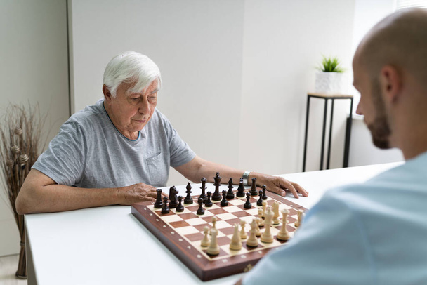 Elderly Senior Playing Chess With Caregiver At Home - Fotoğraf, Görsel
