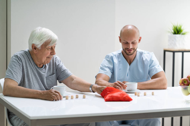Aîné âgé jouant Lotto avec le soignant à la maison - Photo, image