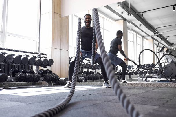 african-american man doing battle rope exercises in fitness gym - Foto, imagen