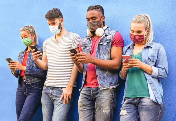 Grupa osób korzystających ze smartfonów w technologii covid 19 razy chronionej maską do twarzy - Przyjaciele sprawdzający wiadomości online stojąc przy ścianie i trzymając telefony komórkowe - Zdjęcie, obraz