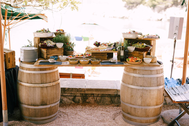 Імпровізований стіл з двох винних бочок та дерев'яний бар з делікатесами та квітами
. - Фото, зображення