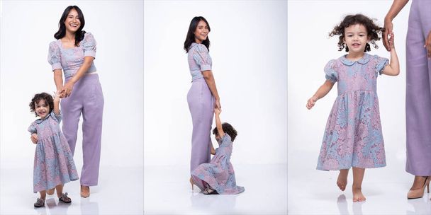 Madre asiática e hija caucásica se paran y usan el mismo vestido de pantalón de blusa púrpura juntos. Niña toma a mamá de la mano y sonríe con amor. Fondo blanco aislado - Foto, imagen