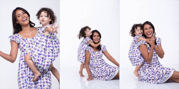 Asijské Matka a Kavkazský Dcera stojí a nosit stejné fialové květinové halenky šaty dohromady. Holčička drží mámu za ruku a usmívá se láskou. izolované bílé pozadí - Fotografie, Obrázek